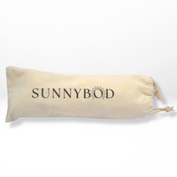 The picture shows an off white cotton fabric SUNNYBOD™ Sunscreen Brush travel Pouch, laying on its side. It has the word "SUNNYBOD" printed in black capital letters vertically down the center. The pouch has a drawstring at the top for opening and closing. The pouch is displayed on a white background.