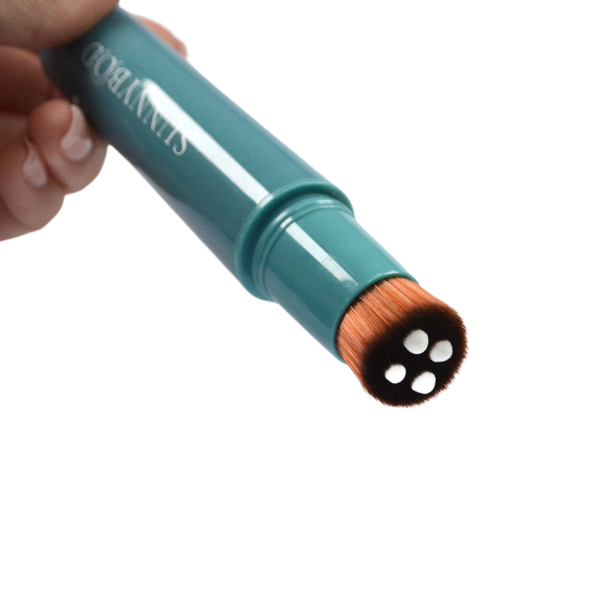 A product picture of a SUNNYBOD™ Refillable Sunscreen Brush Applicator. The brush is turquoise in colour. The susncreen brush bristles are light brown and have droplets of white susncreen dripping from them. The handle has the word "SUNNYBOD" written in white capital letters. The brush is placed on a white background and is being help in the fingertips of well manicured hands.